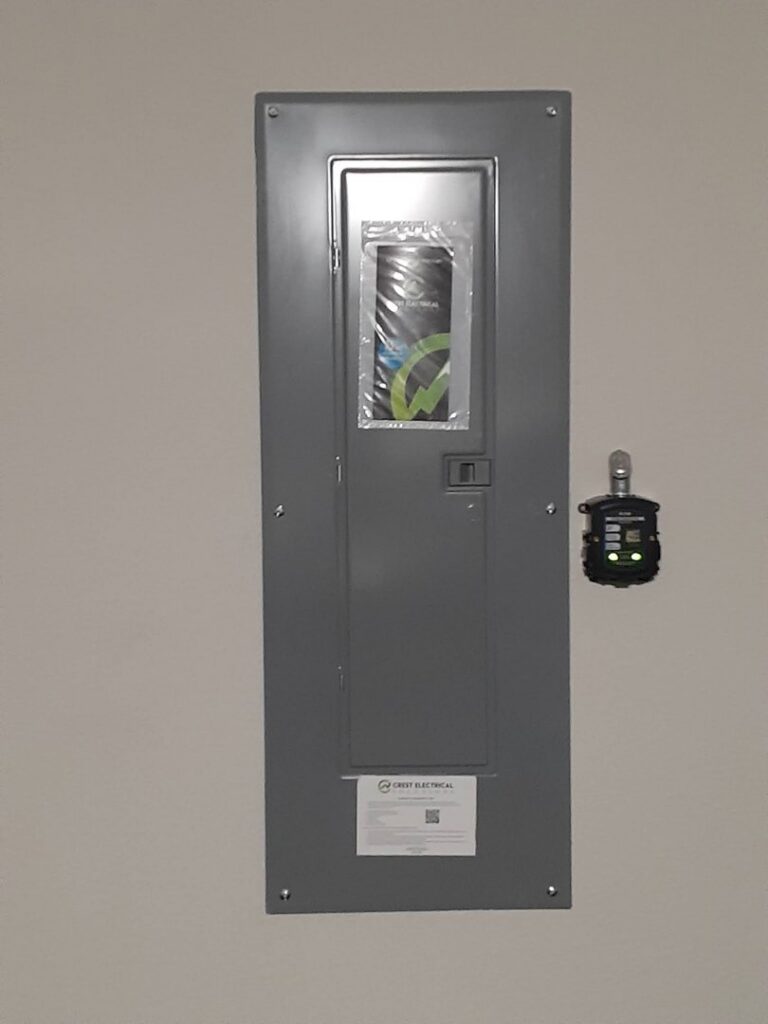 An electrical panel with Crest Electrical Solutions branding and a small device plugged into an adjacent outlet in Arlington, TX.