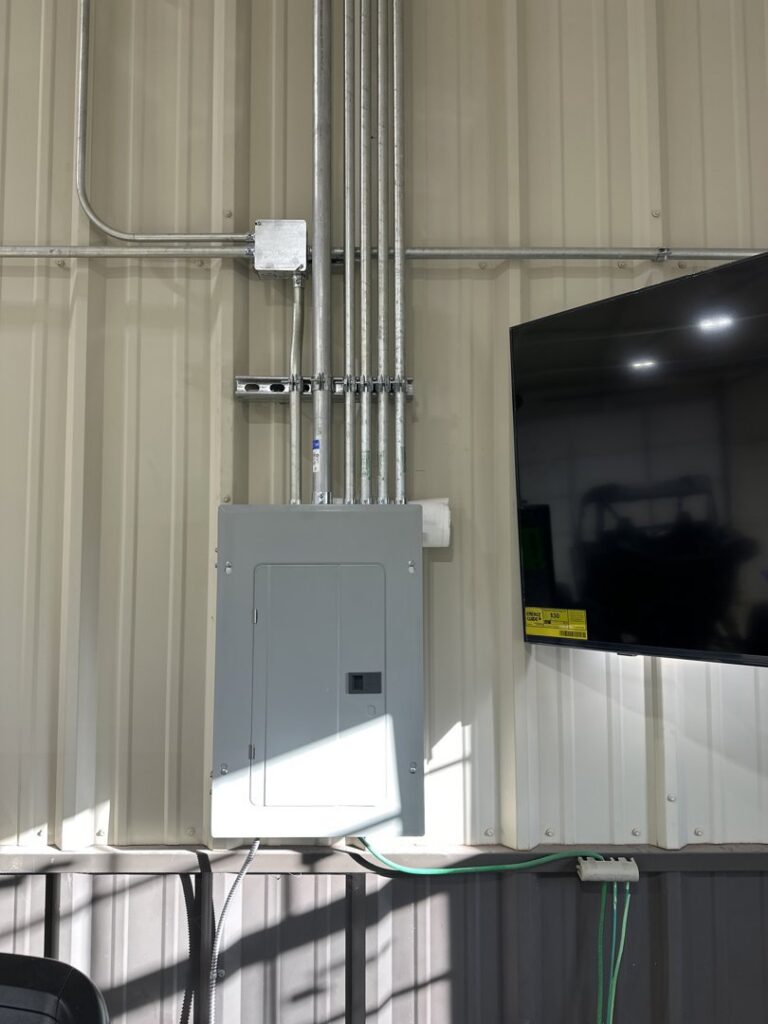 An electrical panel and conduit runs installed on an interior wall next to a television by McLearen Electric in Piedmont, OK.