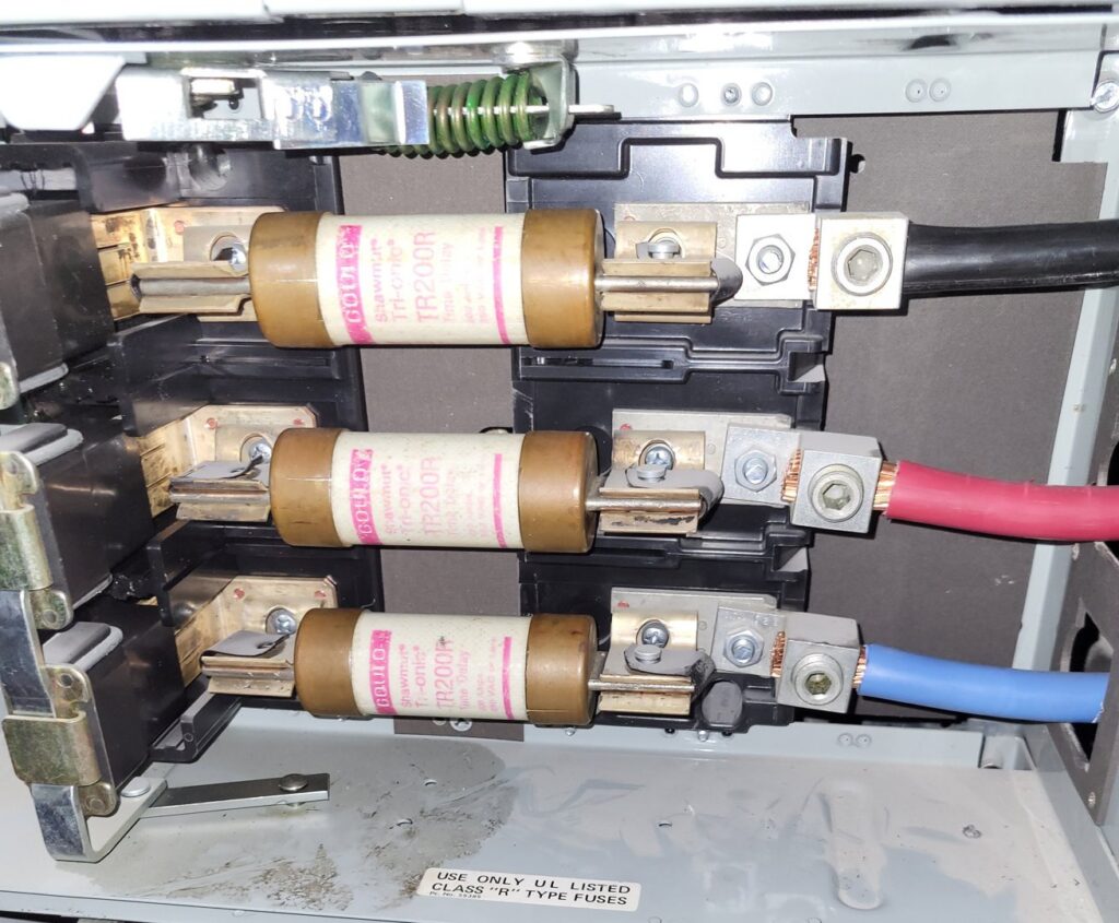 Close-up of large electrical fuses and wiring inside a service panel, maintained by Ozzy Electric in Jacksonville, FL.