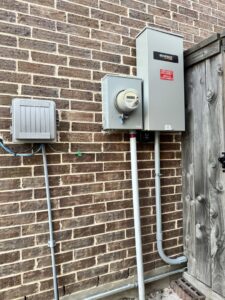 An outdoor electrical panel and Generac transfer switch installed on a brick wall by Never Without Power Generators LLC in Huffman, TX.