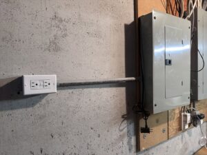A newly installed electrical panel and GFCI outlet on a concrete wall by Mister Sparky Kansas City, MO.