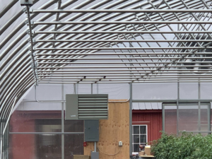 An electrical panel and HVAC unit with visible wiring in a greenhouse, installed by Hulett Electric & Father in Shaftsbury, VT.