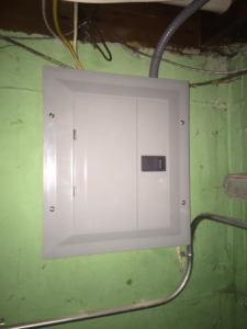 A new electrical panel installed on a green wall, showing professional wiring by Handy Hollms in Waukesha, WI