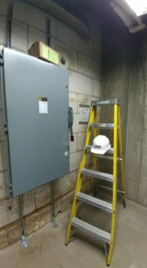 An electrical panel installation with conduit and a hard hat on a ladder by Triumph Electrical Services, Inc in Minneapolis, MN