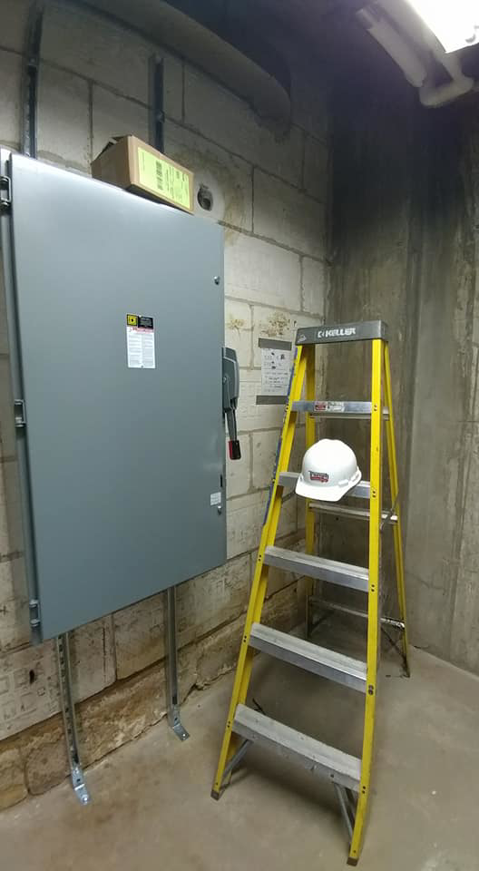 An electrical panel installation with conduit and a hard hat on a ladder by Triumph Electrical Services, Inc in Minneapolis, MN