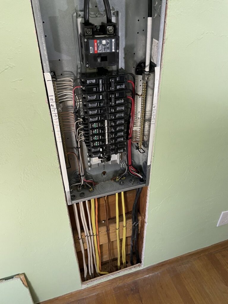 An electrical panel installation with exposed wiring below in a wall by Kot Electric LLC in Kent, WA.