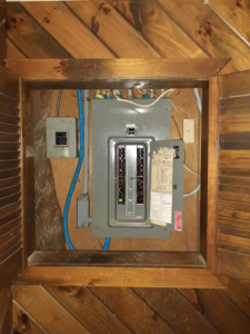 An open electrical panel inside a wooden enclosure, demonstrating an electrical service by Benoit Electrical Services in Litchfield, NH.