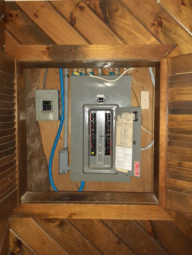An open electrical panel inside a wooden enclosure, demonstrating an electrical service by Benoit Electrical Services in Litchfield, NH.