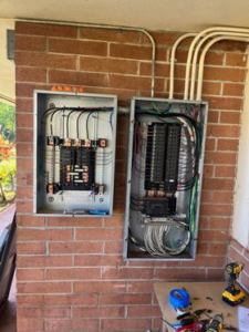 Two electrical panels being wired on a brick wall, with tools nearby, showcasing work by Mcdaniel Electric, LLC in Waipahu, HI.