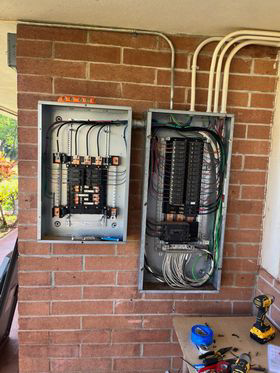 Two electrical panels being wired on a brick wall, with tools nearby, showcasing work by Mcdaniel Electric, LLC in Waipahu, HI.