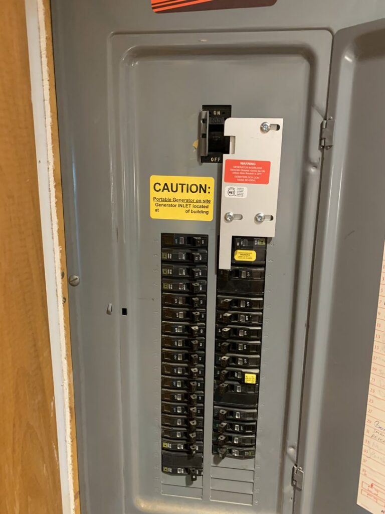 An electrical panel with a generator interlock kit and caution labels installed by Josh LaFerriere Electric in Westbrook, ME.