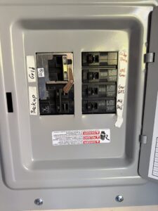 An open electrical sub-panel showing circuit breakers for grid and backup power by TJAM Electric in Springtown, TX.