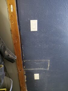 An electrical light switch and outlet installed on a blue wall by LE Electric in Las Cruces, NM