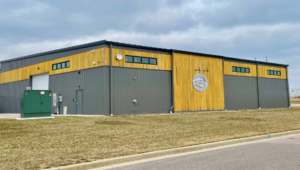 A green electrical utility box outside a commercial building, representing work by Electrical Dimensions, Inc. in Verona, WI.