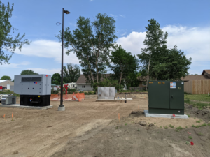 An outdoor installation of electrical utility boxes, a generator, and a street light pole by Burlington Electric in Burlington, ND.