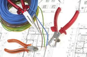 Electrical wires, pliers, and wire strippers laid out on blueprints, demonstrating the work of Corbin & Maille, Inc in Erie, PA.