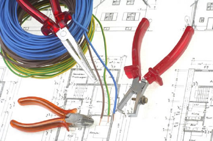 Electrical wires, pliers, and wire strippers laid out on blueprints, demonstrating the work of Corbin & Maille, Inc in Erie, PA.