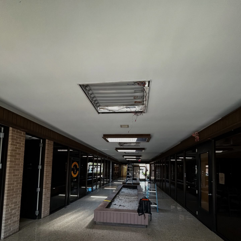 An open ceiling panel revealing electrical wiring and light fixture installation in a commercial hallway by Mechatronics LLC in Memphis, TN.