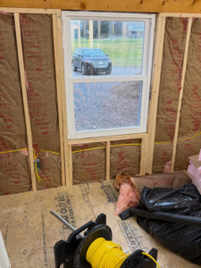 Electrical wiring installation along a wall with insulation and a spool of wire by J's Electrical & Maintenance Services, LLC in Columbus, OH.