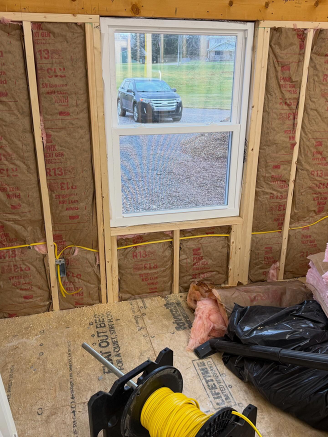 Electrical wiring installation along a wall with insulation and a spool of wire by J's Electrical & Maintenance Services, LLC in Columbus, OH.