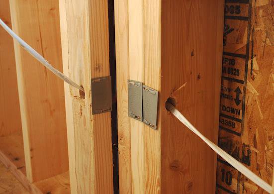 Electrical wiring running through wooden studs in a wall with protective plates, showing rough-in work by Affordable Electric, LLC in Kearney, NE.