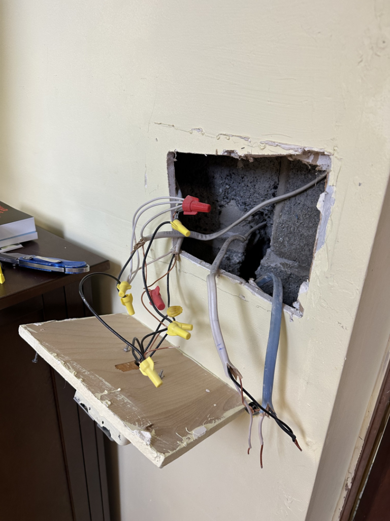 Electrical wiring with wire nuts exposed in a wall opening, showing work by Watts Happening Electric in Lakewood, CO.