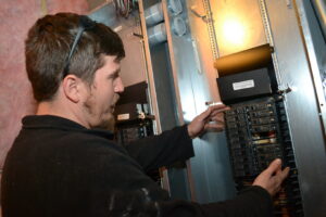 An electrician adjusting components inside an electrical panel, performing service for Rebco Electric in Lebanon, OH.