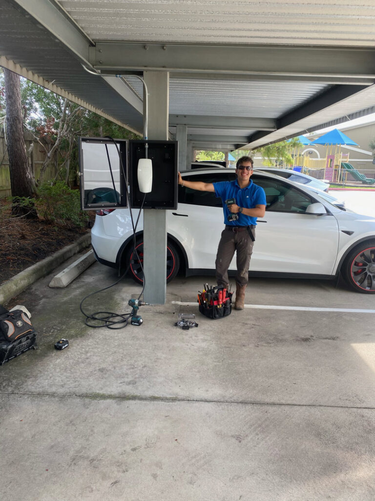 An Ultralight Electrician standing proudly next to a newly installed EV charging station for a Tesla in Houston, TX.