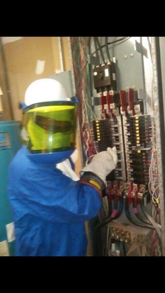 An electrician in arc flash PPE working on an industrial electrical panel for Professional Electric in Mobile, AL