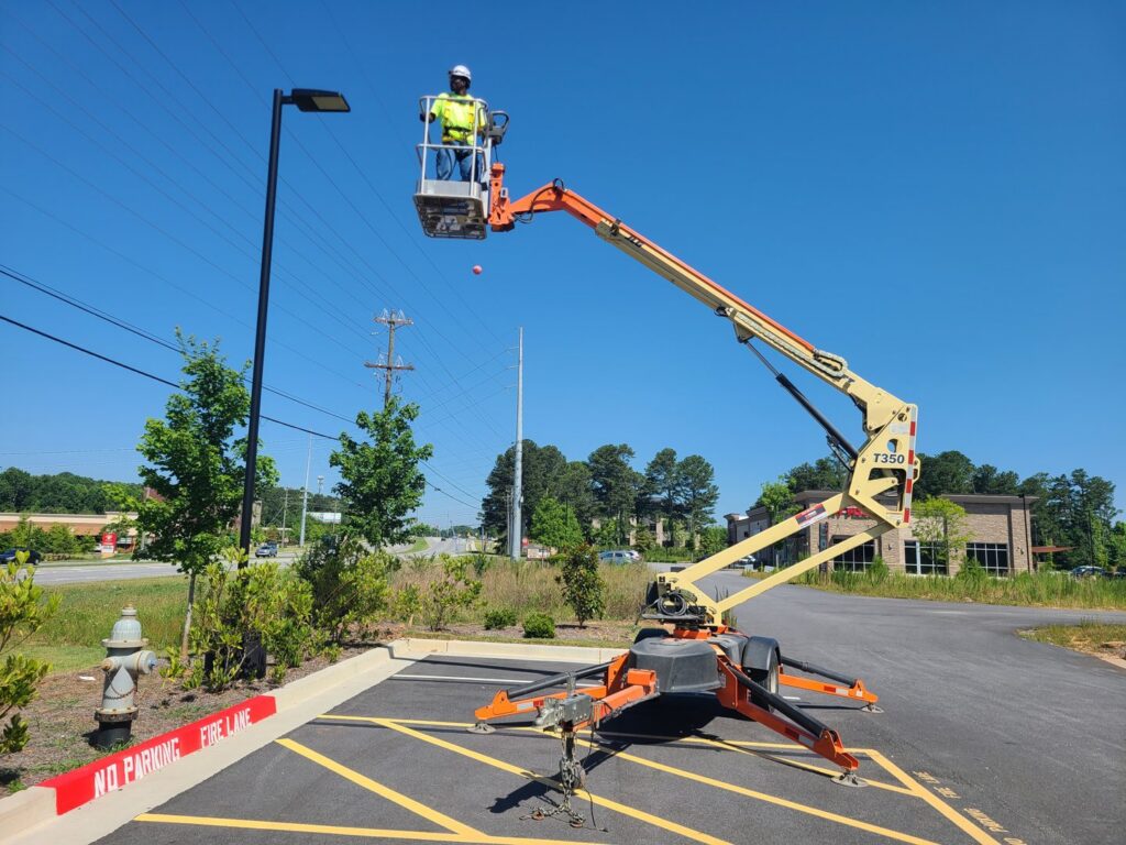 An electrician in a boom lift performing outdoor light pole repair, a service offered by 8Thirty Electric, Inc. in Johns Creek, GA.