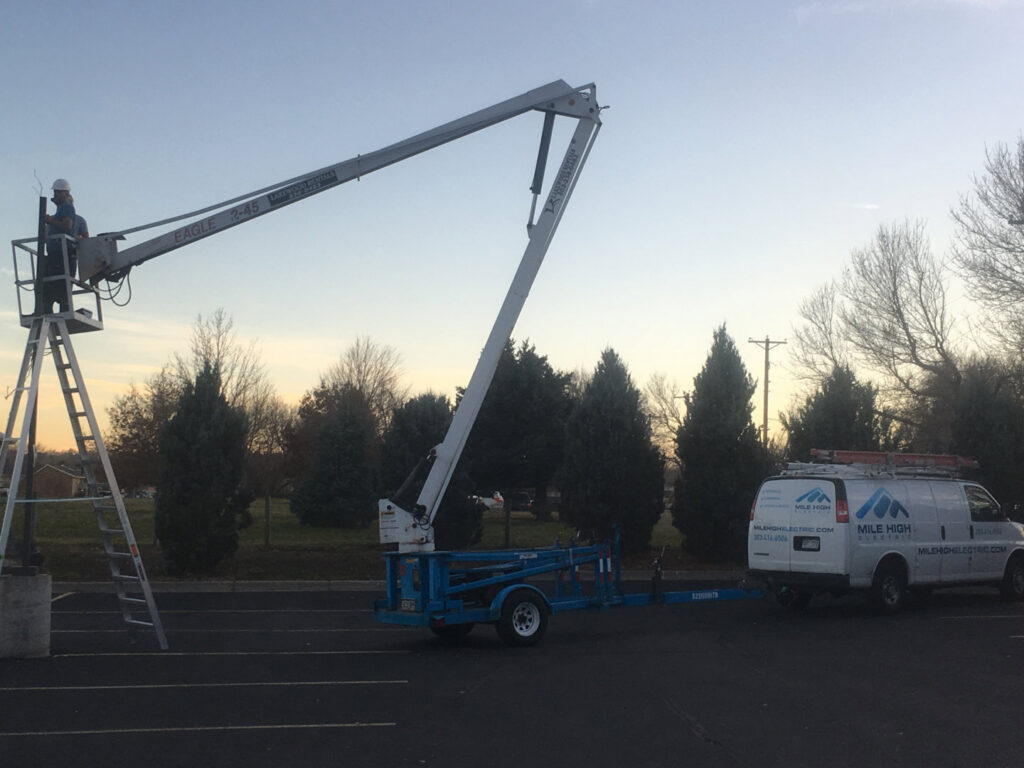 An electrician in a boom lift working on outdoor electrical components for Mile High Electric in Denver, CO