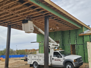 An electrician in a bucket truck working on roof wiring at a construction site for Colonial Electric LLC in Scottsdale, AZ.