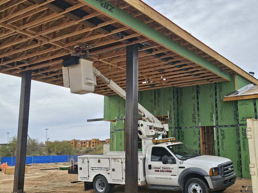 An electrician in a bucket truck working on roof wiring at a construction site for Colonial Electric LLC in Scottsdale, AZ.