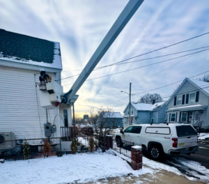 An electrician in a bucket truck performing residential electrical service work for East West Electric LLC in Chester, NH.