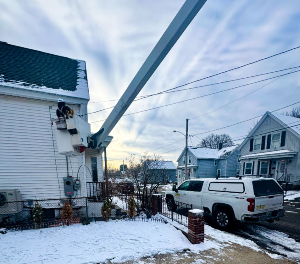An electrician in a bucket truck performing residential electrical service work for East West Electric LLC in Chester, NH.