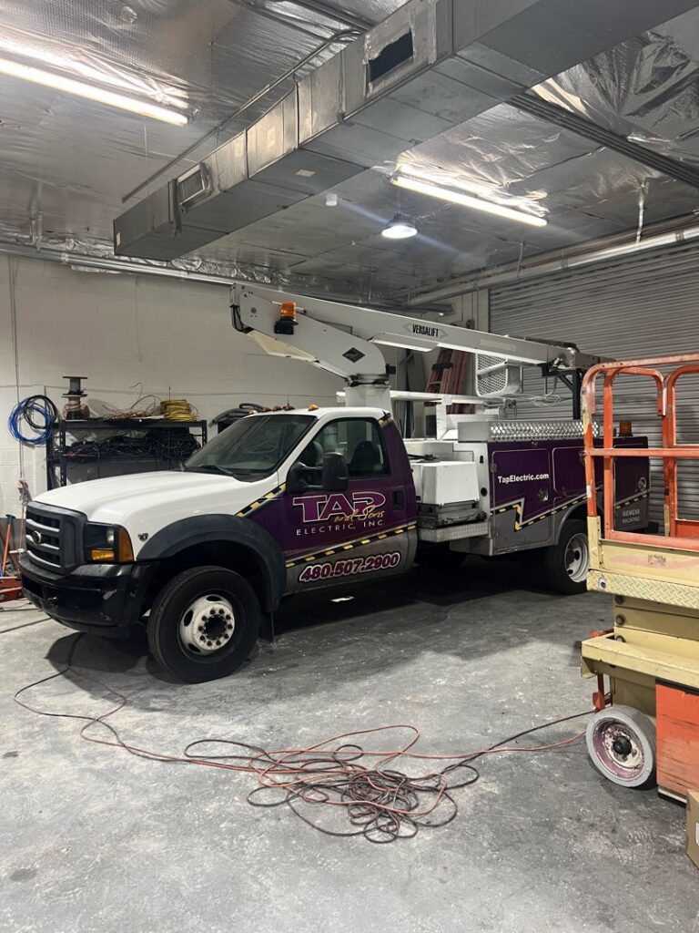 An electrician's bucket truck from TAP and Sons Electric parked in a garage in Tempe, AZ, ready for service.
