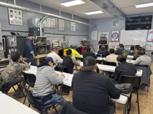 An electrician classroom with students seated at desks and electrical training panels visible on the wall at Escuela Tecnica ABC in North Chicago, IL