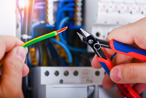 An electrician's hands cutting an electrical wire with wire cutters near an electrical panel for BrotherlyLove Electric LLC in Houston, TX.