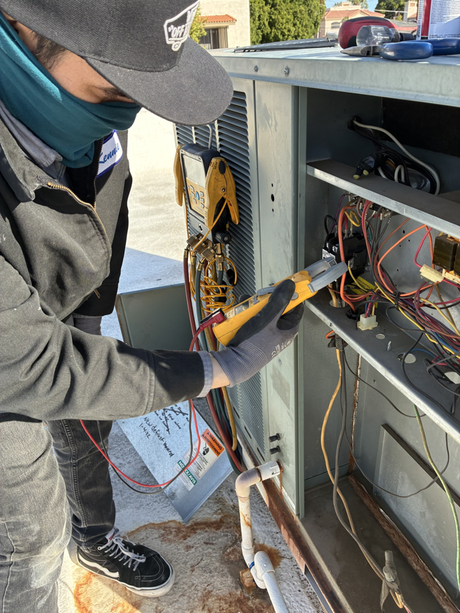 An electrician diagnosing an AC unit's electrical panel with a multimeter for Cool Aid Air Conditioning in Scottsdale, AZ