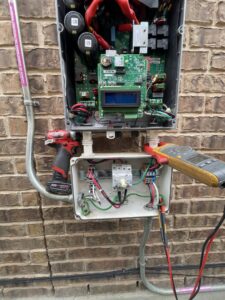 An electrician diagnosing an open electrical inverter or control box with a multimeter for Rubio Electrical Innovations LLC in San Antonio, TX.