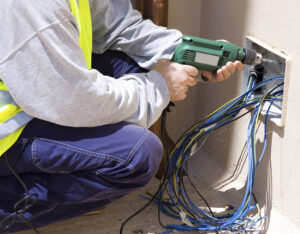 An electrician drilling into a wall to install new wiring for Mulholland Electric Inc in San Francisco, CA.