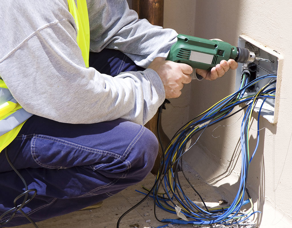 An electrician drilling and installing electrical wires into a wall box for OMR Electrical Contractors Inc. in Cape Coral, FL.
