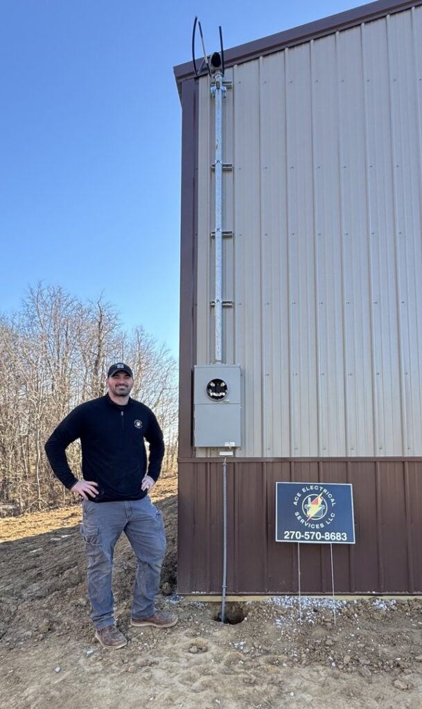 An electrician from Ace Electrical Services LLC standing next to a newly installed electrical meter and conduit on a building in Owensboro, KY.