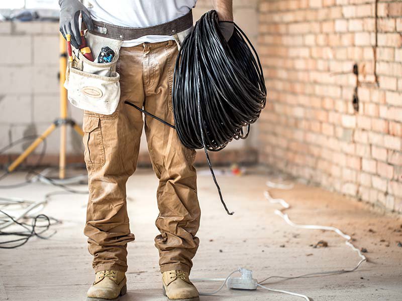 An electrician holding a coil of black electrical wire, ready for installation by Omni Power Electrical Services LLC in San Antonio, TX