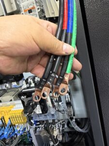 An electrician's hand holding thick electrical wires with terminals for Pioneer Electric LLC in West Valley City, UT.