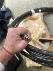 An electrician's hand holding a thick electrical cable with exposed copper wires, demonstrating expertise from MLEC in Annapolis, MD