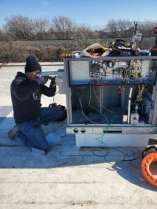 An electrician performing repair or maintenance on an HVAC unit on a rooftop for Genesys Electrical Contractors in Dallas, TX