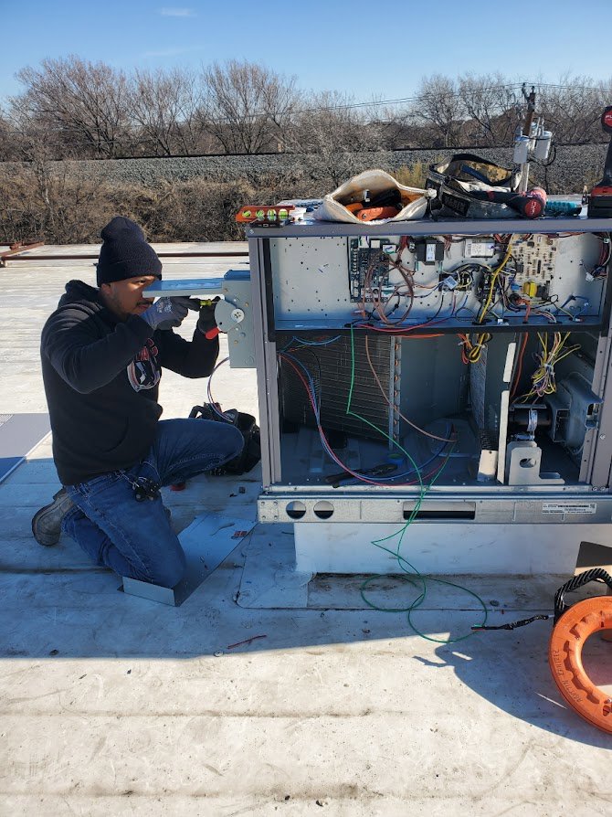 An electrician performing repair or maintenance on an HVAC unit on a rooftop for Genesys Electrical Contractors in Dallas, TX