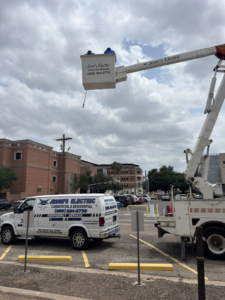 An electrician from Jesse's Electric working from a bucket truck with a company van parked nearby in Laredo, TX.