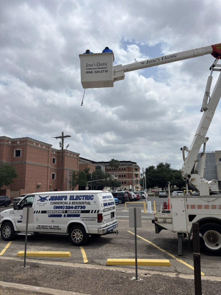 An electrician from Jesse's Electric working from a bucket truck with a company van parked nearby in Laredo, TX.